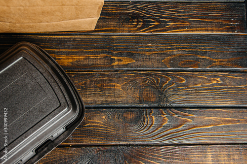 Tablou pe pânză A brown craft paper bag and a black container for taking out or delivering goods and food on a wooden table