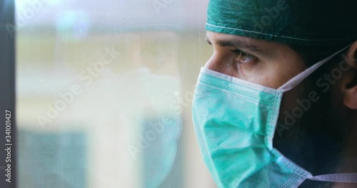 Medico o infermiere uomo con cuffia e mascherina guarda stanco fuori dalla finestra. photo