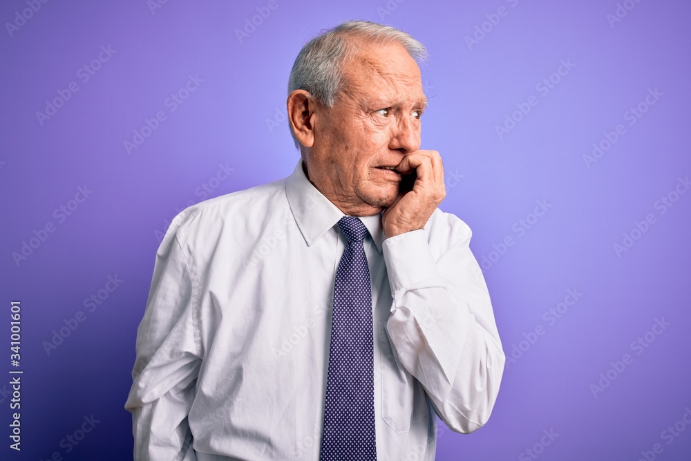 Grey haired senior business elegant man standing over purple isolated background looking stressed and nervous with hands on mouth biting nails. Anxiety problem. Grey haired senior business elegant man standing over purple isolated background looking stressed and nervous with hands on mouth biting nails. Anxiety problem.