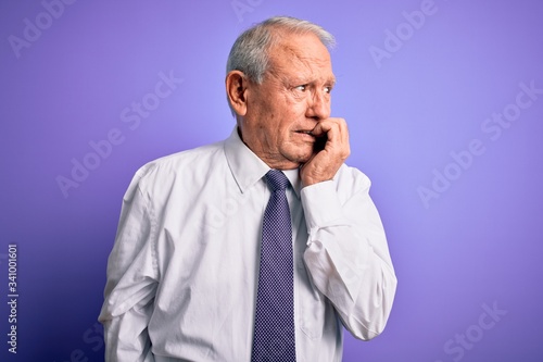 Grey haired senior business elegant man standing over purple isolated background looking stressed and nervous with hands on mouth biting nails. Anxiety problem. © Krakenimages.com