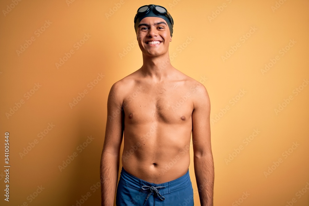 Young handsome man shirtless wearing swimsuit and swim cap over isolated yellow background with a happy and cool smile on face. Lucky person.