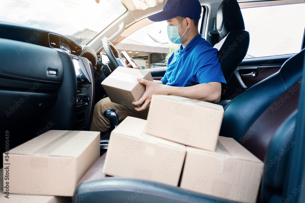Asian Delivery man wearing mask send a package holding smartphone on front home receiver shipping deliver cargo social distancing, Many parcel in hatchback car while the virus is spreading medical. Asian Delivery man wearing mask send a package holding smartphone on front home receiver shipping deliver cargo social distancing, Many parcel in hatchback car while the virus is spreading medical.