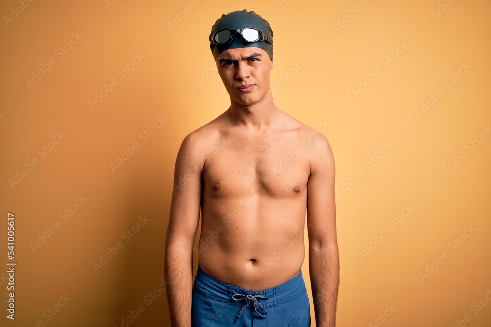 Young handsome man shirtless wearing swimsuit and swim cap over isolated yellow background skeptic and nervous, frowning upset because of problem. Negative person.