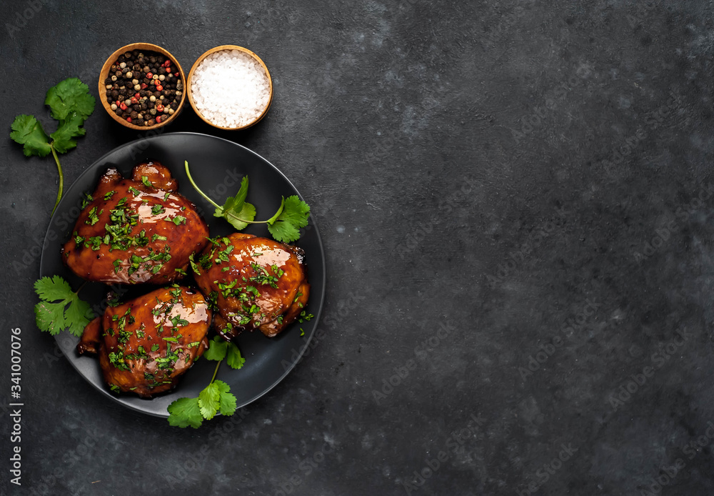 Grilled sweet chicken thighs with herbs and spices on a black plate on a stone background with copy space for your text