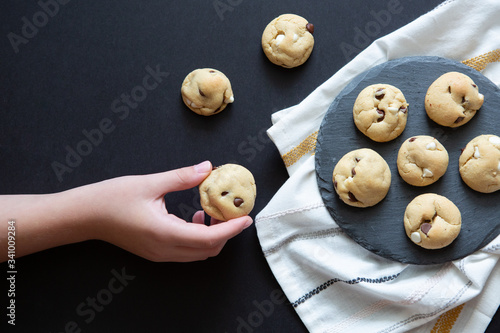 Hand Reaching For Chocolate Chip Cookies On Slate Platter With Black Background