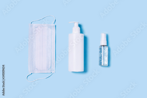 Flat lay with a medical mask placed in the center  a bottle of antiseptic soap and a hand sanitizer.