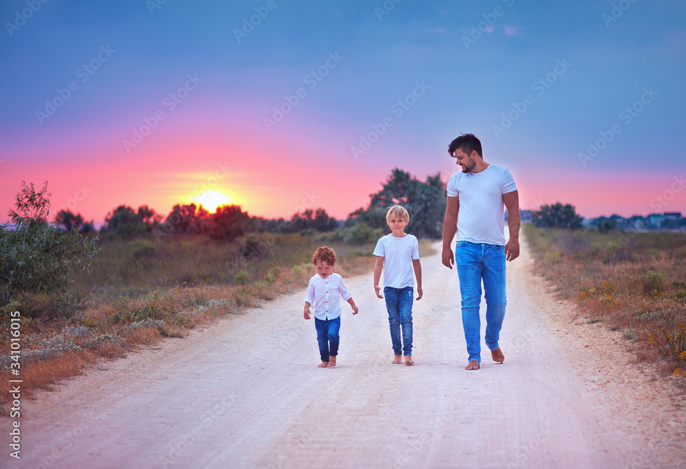 barefoot father and sons walking together along a countryside summer road at sunset. happy family barefoot father and sons walking together along a countryside summer road at sunset. happy family