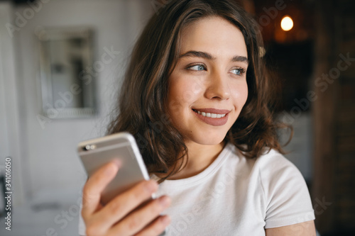 Charming young European woman with blue eyes messaging boyfriend via online app on her mobile, flirting, looking away with dreamy smile, planning trip together after social distancing period © Anatoliy Karlyuk