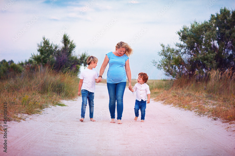 young pregnant woman walking together with two sons. Happy family on summer sandy path young pregnant woman walking together with two sons. Happy family on summer sandy path
