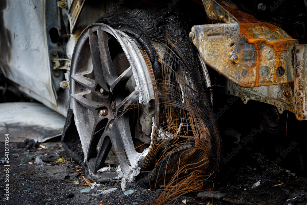 Wheel of burned car. Burnt flat tire on the car is on the gray asphalt road. Wheel of burned car. Burnt flat tire on the car is on the gray asphalt road.