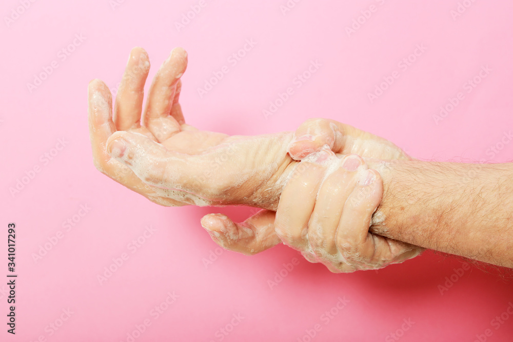 Fototapeta premium manos de hombre lavándose con jabón sobre fondo rosa.