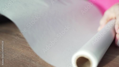 The housewife unwraps a roll of baking paper on a wooden table. Cooking at home, in the kitchen