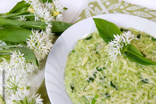 Ramsons (wild garlic leek ) risotto with parmesan cheese, served in a white plate with fresh ramson leaves and flowers as decoration photo