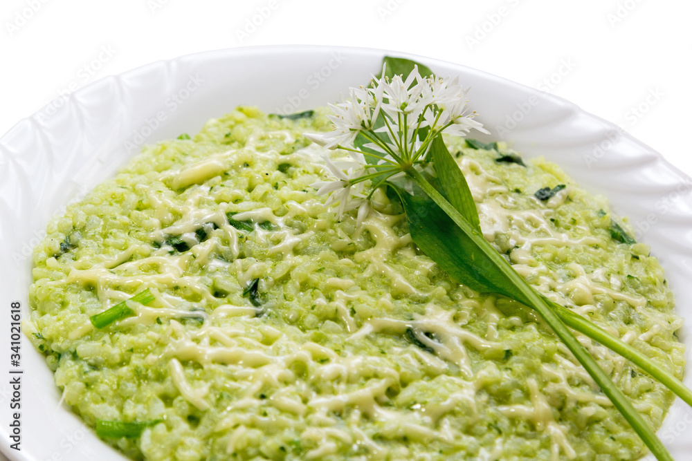 Ramsons (wild garlic leek ) risotto with parmesan cheese, served in a white plate with fresh ramson leaves and flowers as decoration on white background
