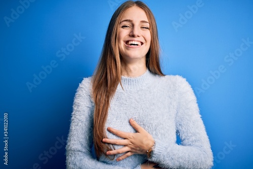 Young beautiful redhead woman wearing casual sweater over isolated blue background smiling and laughing hard out loud because funny crazy joke with hands on body. © Krakenimages.com