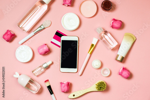 Concept of online shopping cosmetics. Top view on cosmetics bottles, cream, soap, makeup brushes, mobile phone on a pink background, flat lay,