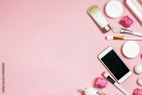 Concept of online shopping cosmetics. Top view on cosmetics bottles, cream, soap, makeup brushes, mobile phone on a pink background, flat lay, frame