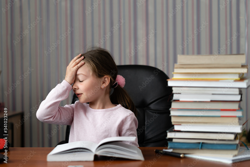 Online distance learning concept. Little schoolgirl is sitting at home near the laptop, a pile of books nearby. Online distance learning concept. Little schoolgirl is sitting at home near the laptop, a pile of books nearby.