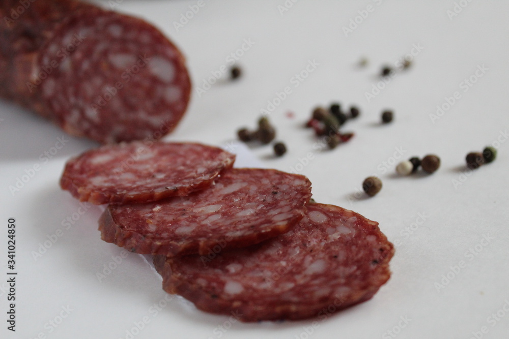a stick and sliced pieces of smoked sausage lies on a white background next to the pepper peas black white red in the background pepper and baguette