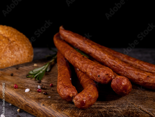 Smoked pork sausage in composition with fresh herbs, bread, wood cutting board and jute fabric.