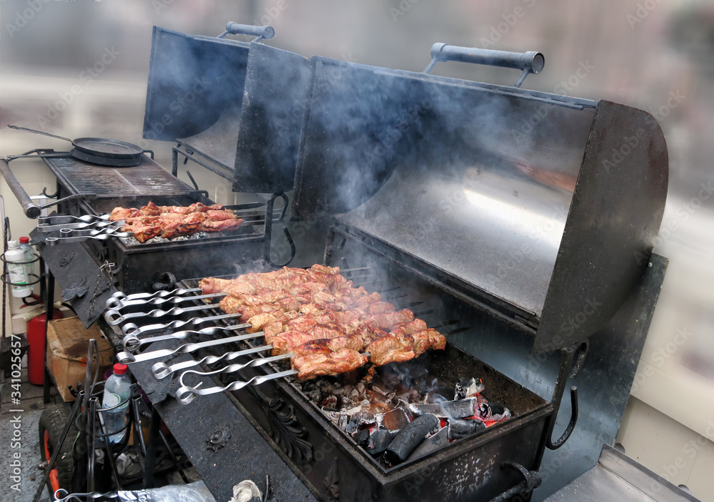 Meat with smoke on a barbecue grill over charcoal. Grilled cubes of meat on metal skewer. Meat on skewers is roasted on fire. Meat with smoke on a barbecue grill over charcoal. Grilled cubes of meat on metal skewer. Meat on skewers is roasted on fire.