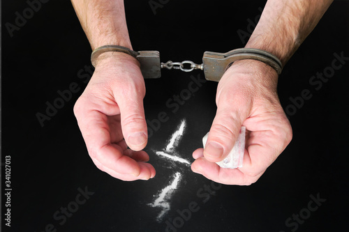 Police handcuffs on men's hands, heroin, cocaine powder and a bag of the substance. Punishment for drug distribution.