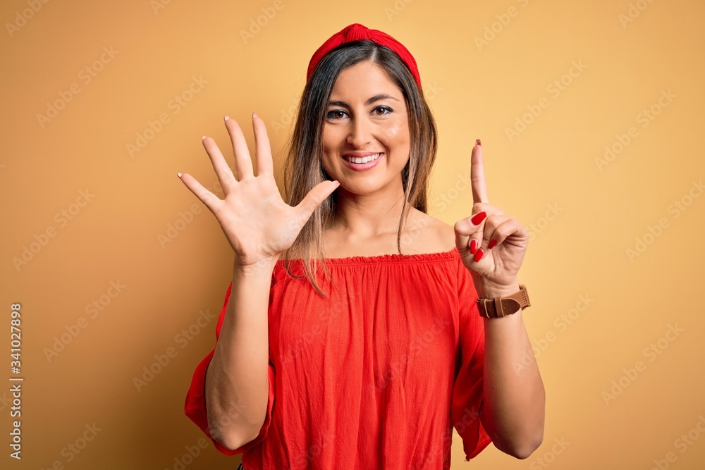 Young beautiful woman colorful summer style over yellow isolated background showing and pointing up with fingers number six while smiling confident and happy. Young beautiful woman colorful summer style over yellow isolated background showing and pointing up with fingers number six while smiling confident and happy.
