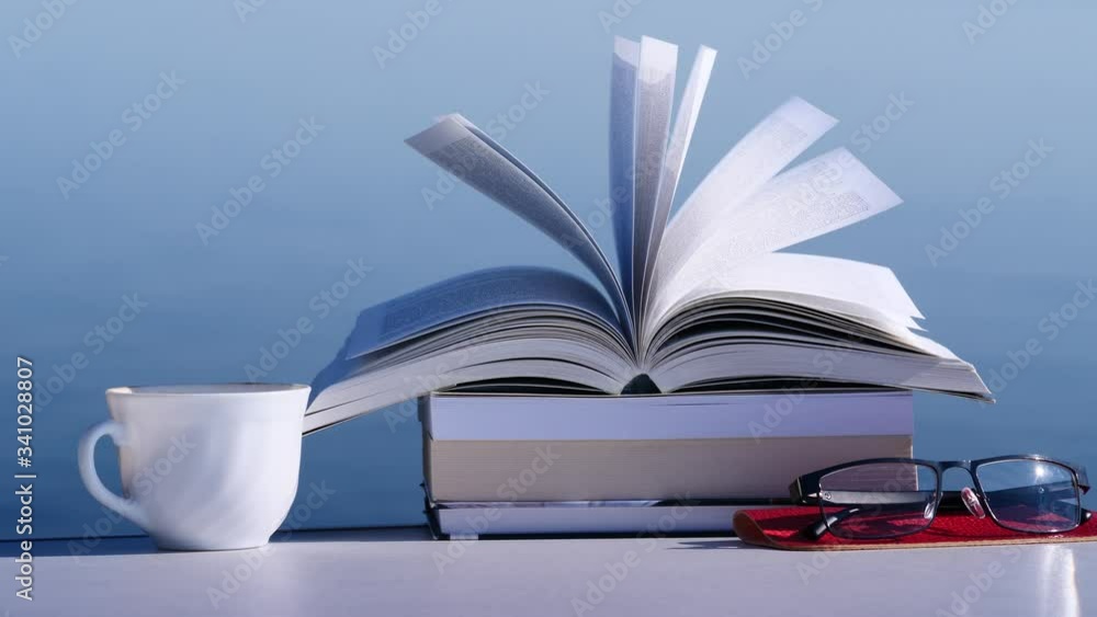 Reading on holidays. Coffee cup and books on table outdoors against blue sea water background. Book pages fluttering in the wind Reading on holidays. Coffee cup and books on table outdoors against blue sea water background. Book pages fluttering in the wind