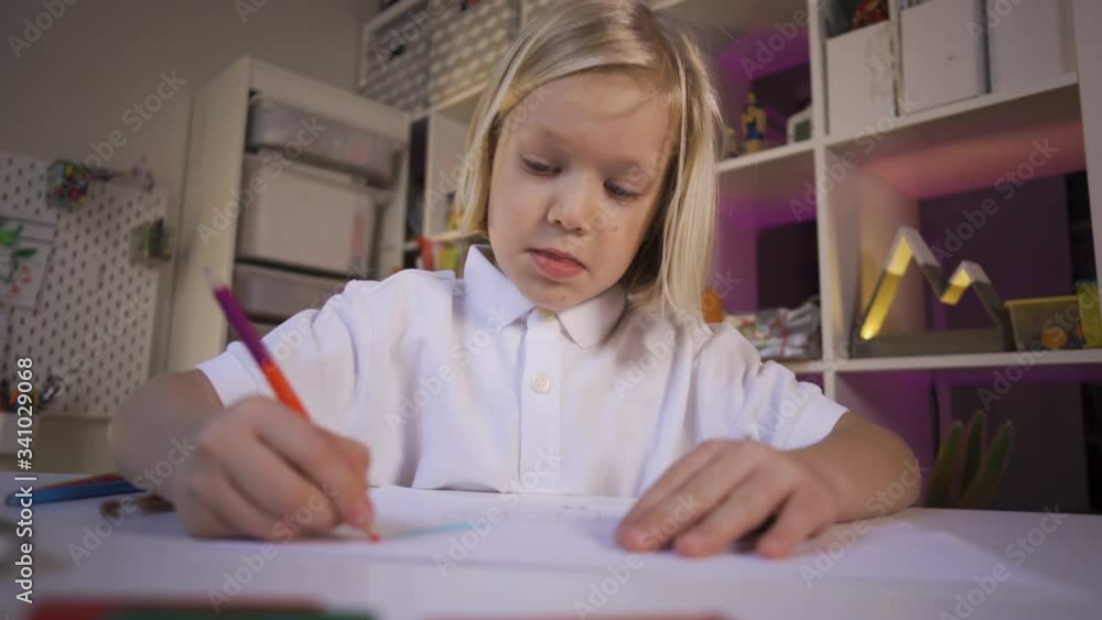 Distance learning due quarantine, online education. Long blond hair preschooler boy in white shirt watching something on the laptop device at the desk in the cozy kid's room. Distance learning due quarantine, online education. Long blond hair preschooler boy in white shirt watching something on the laptop device at the desk in the cozy kid's room.