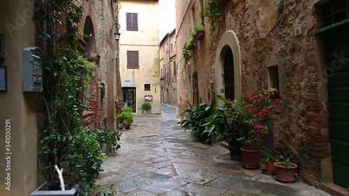 Smooth camera steady slide shot around old Tuscany village Pienza narrow empty streets, with old stone walls, shelled facades with flowers, early in the morning