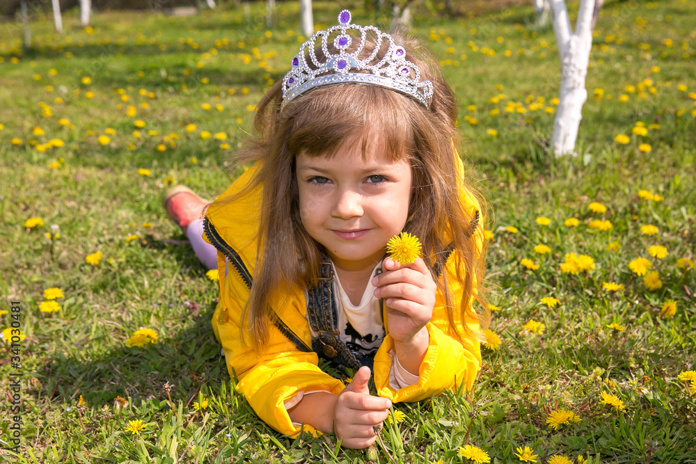 Little girl baby in yellow clothes lies on green grass and lots of dandelions Little girl baby in yellow clothes lies on green grass and lots of dandelions