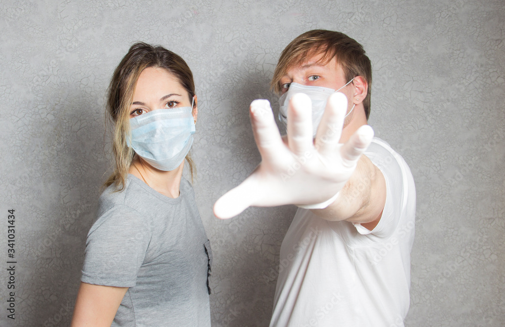 A man and a woman in masks and gloves show the stop. A man in a medical mask shows a hand gesture keep your distance. Selective focus. A man and a woman in masks and gloves show the stop. A man in a medical mask shows a hand gesture keep your distance. Selective focus.