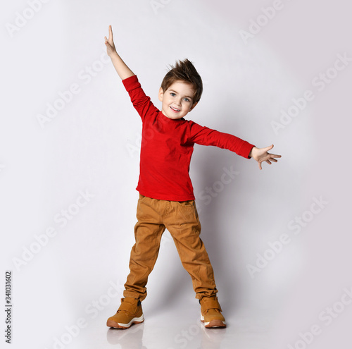 Little boy kid child, stylish hairstyle in sunglasses, red jumper smiling spread hands, pointing fingers showing tongue posing photo