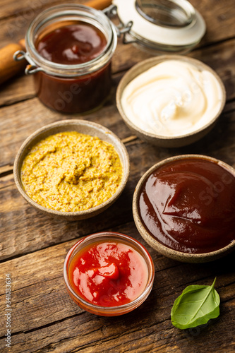 Classic set of sauces, American yellow mustard, ketchup, barbecue sauce, mayonnaise on wooden background, top view with copy space.
