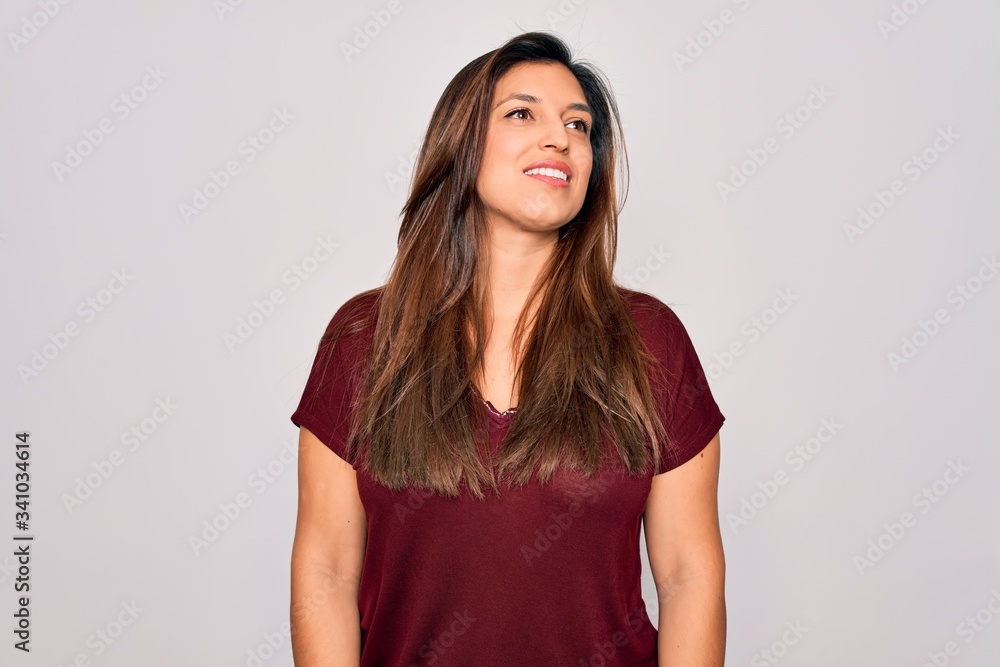 Young hispanic woman wearing casual t-shirt standing over isolated background looking away to side with smile on face, natural expression. Laughing confident. Young hispanic woman wearing casual t-shirt standing over isolated background looking away to side with smile on face, natural expression. Laughing confident.