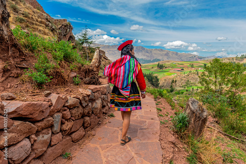 Quechua Indigenous Woman in traditional clothes walking along ancient Inca Wall in the ruin of Tipon, Cusco, Peru.
