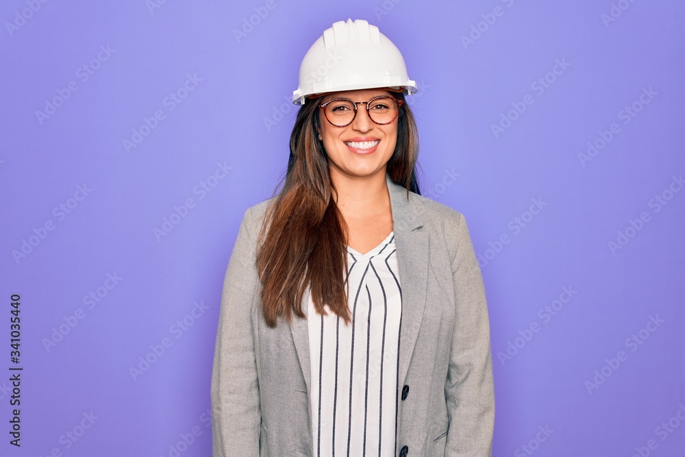 Professional woman engineer wearing industrial safety helmet over pruple background with a happy and cool smile on face. Lucky person.