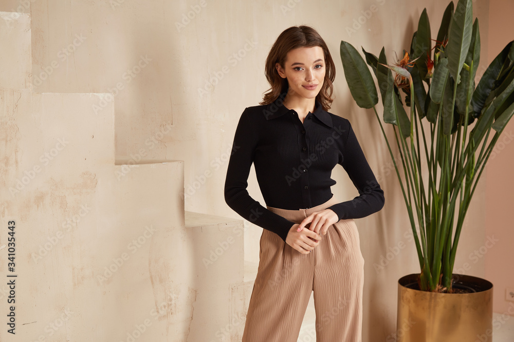 Beautiful brunette woman natural make up wear fashion clothes casual dress  code office style black blouse and beige pants suit for romantic date  business meeting accessory interior stairs flowerpot. Stock Photo