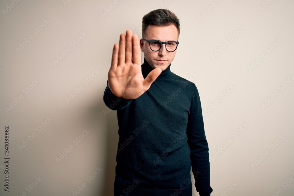 Young handsome caucasian man wearing glasses and casual sweater over isolated background doing stop sing with palm of the hand. Warning expression with negative and serious gesture on the face. Young handsome caucasian man wearing glasses and casual sweater over isolated background doing stop sing with palm of the hand. Warning expression with negative and serious gesture on the face.