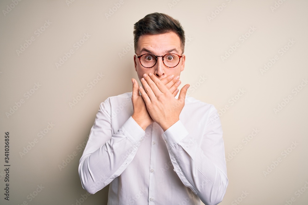 Young handsome business mas wearing glasses and elegant shirt over isolated background shocked covering mouth with hands for mistake. Secret concept. Young handsome business mas wearing glasses and elegant shirt over isolated background shocked covering mouth with hands for mistake. Secret concept.