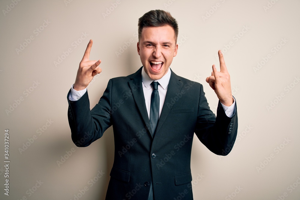 Young handsome business man wearing elegant suit and tie over isolated background shouting with crazy expression doing rock symbol with hands up. Music star. Heavy music concept. Young handsome business man wearing elegant suit and tie over isolated background shouting with crazy expression doing rock symbol with hands up. Music star. Heavy music concept.