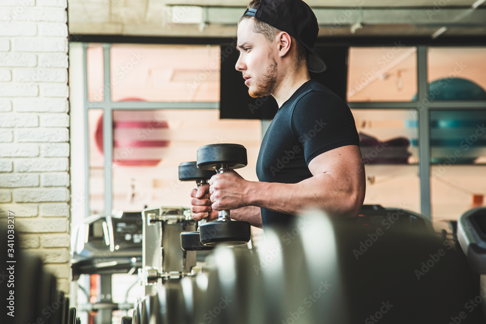Portrait of a muscular man performs exercises in the gym. Strength training with dumbbells Portrait of a muscular man performs exercises in the gym. Strength training with dumbbells
