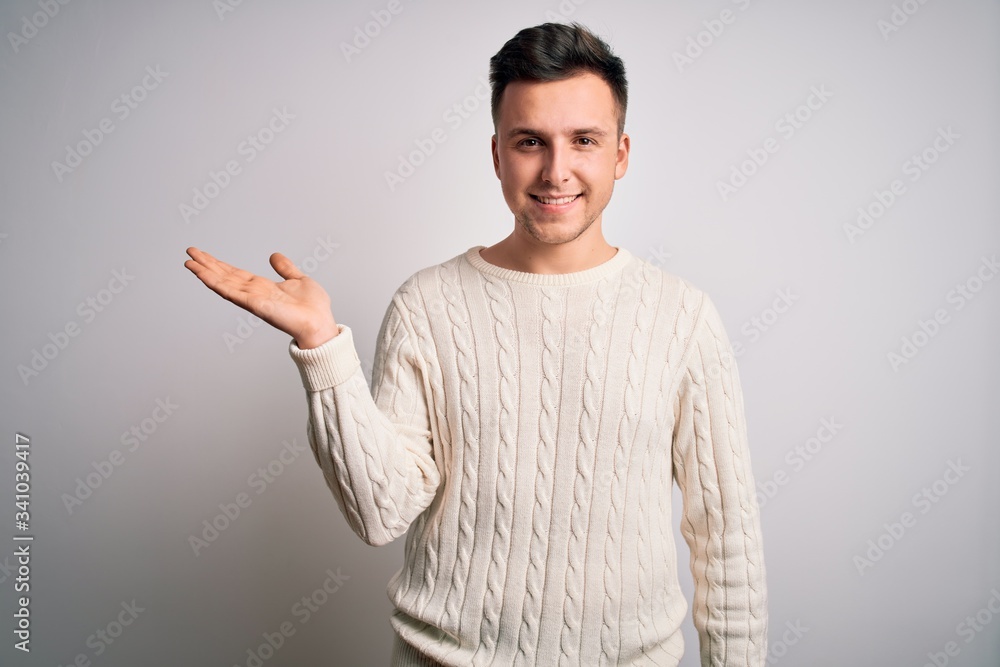 Young handsome caucasian man wearing casual winter sweater over white isolated background smiling cheerful presenting and pointing with palm of hand looking at the camera. Young handsome caucasian man wearing casual winter sweater over white isolated background smiling cheerful presenting and pointing with palm of hand looking at the camera.