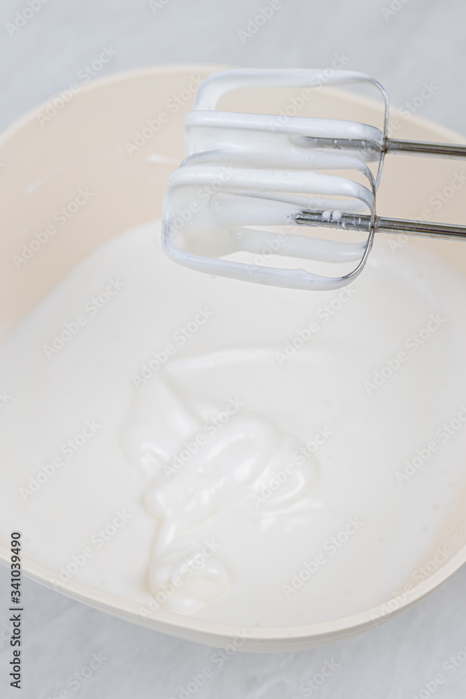 White whipped cream in the bowl with mixer above White whipped cream in the bowl with mixer above