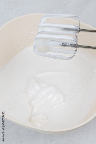 White whipped cream in the bowl with mixer above