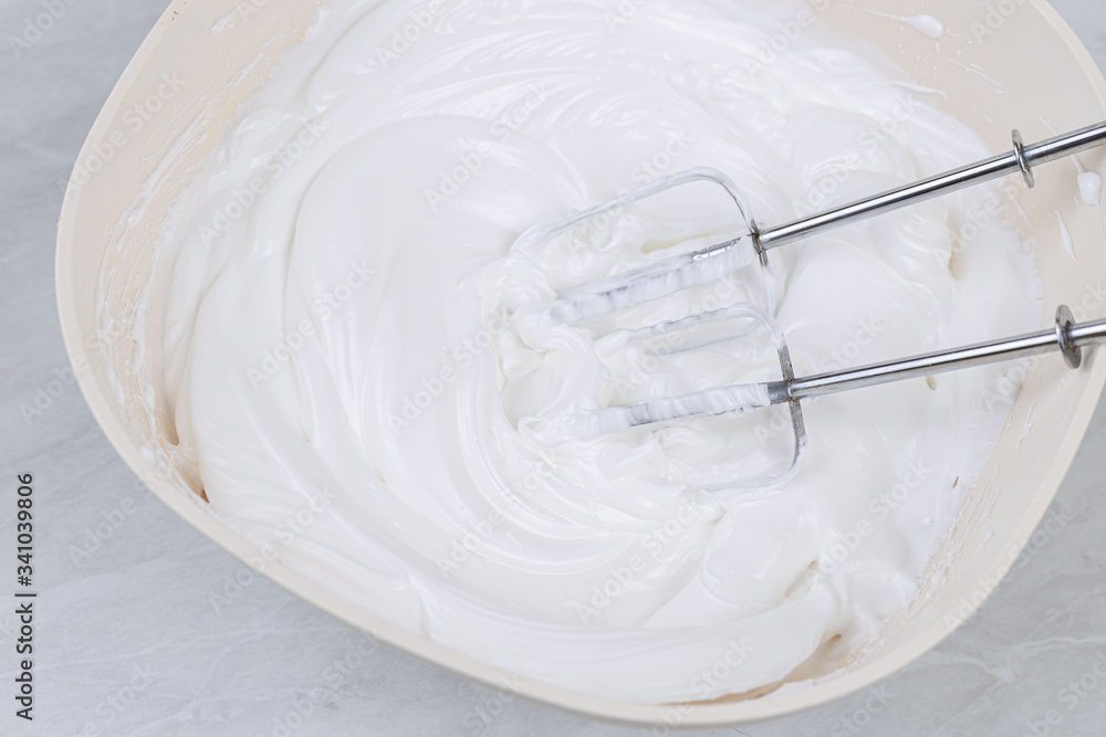 White whipped cream in the bowl with mixer above White whipped cream in the bowl with mixer above