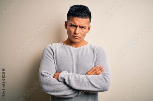 Young handsome latin man wearing casual sweater standing over isolated white background skeptic and nervous, disapproving expression on face with crossed arms. Negative person. © Krakenimages.com