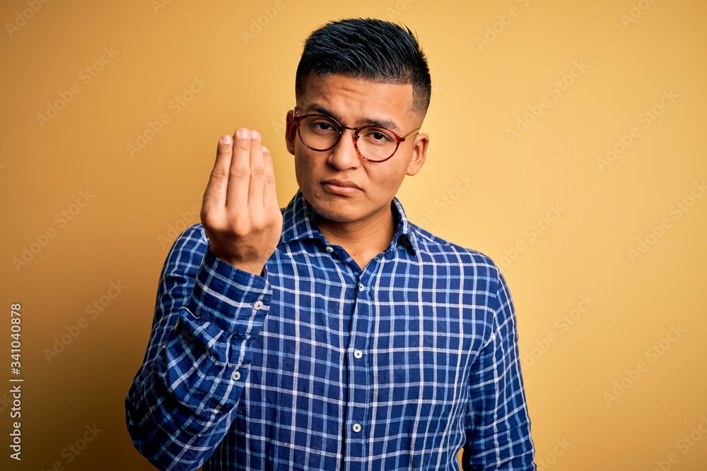 Young handsome latin man wearing casual shirt and glasses over yellow background Doing Italian gesture with hand and fingers confident expression Young handsome latin man wearing casual shirt and glasses over yellow background Doing Italian gesture with hand and fingers confident expression