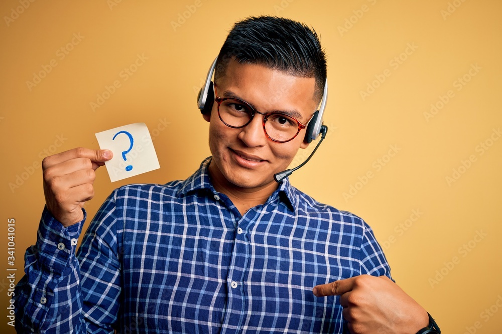 Young latin call center agent man holding question mark reminder paper using headset with surprise face pointing finger to himself Young latin call center agent man holding question mark reminder paper using headset with surprise face pointing finger to himself