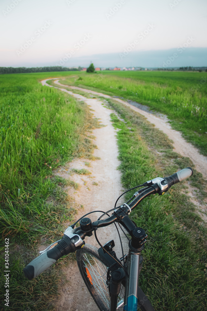 Bicycle steering wheel and gravel road in green summer field Bicycle steering wheel and gravel road in green summer field